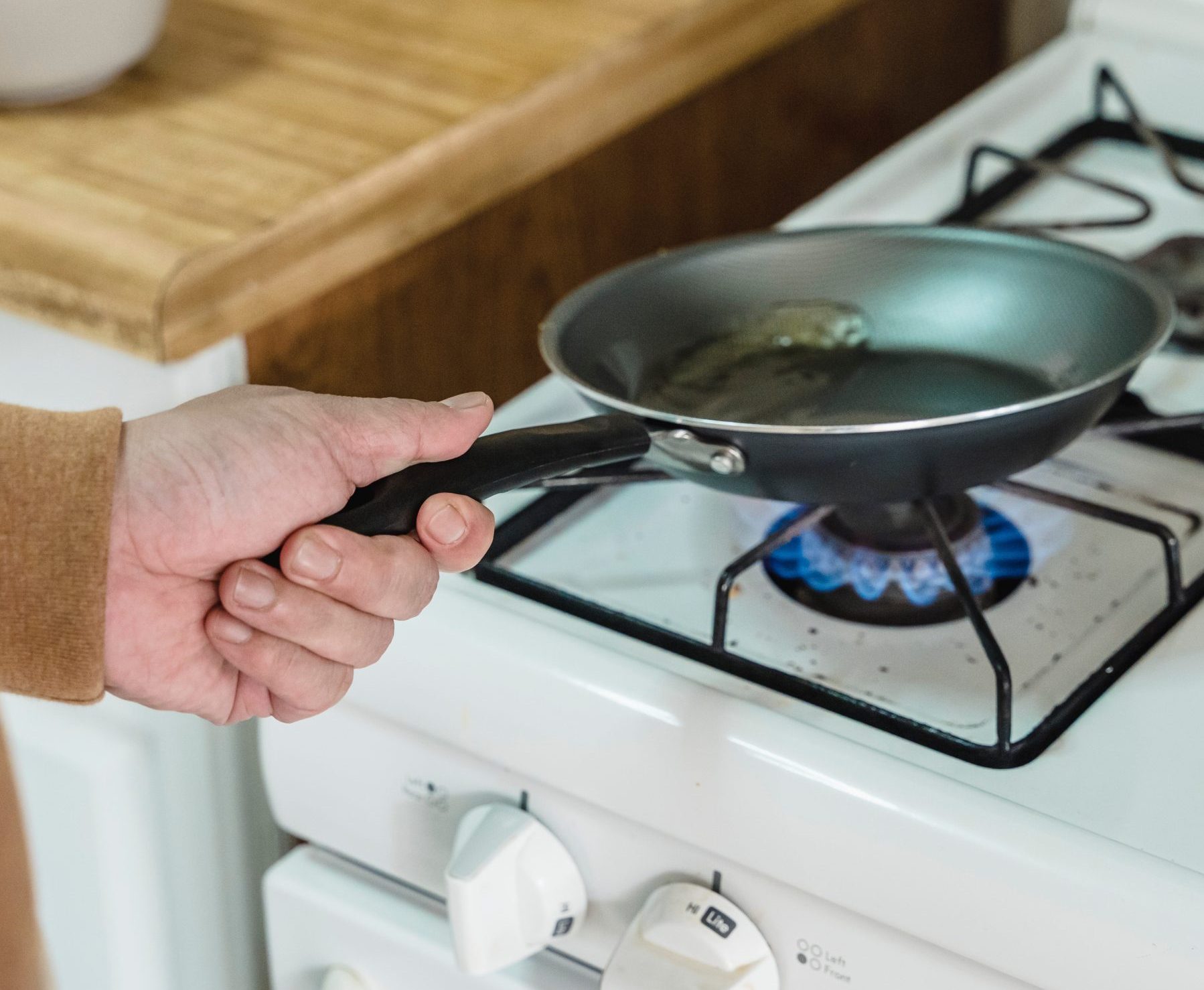 White hand holding handle of frying pan over a gas fire hob